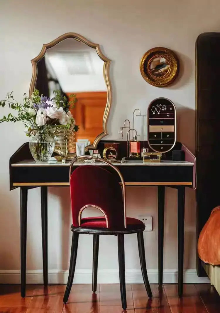 Une chaise rembourrée en velours bordeaux avec des pieds en bois noir et un dossier incurvé, complétant une décoration murale ovale dorée ornementale de miroirs de salle de bains, reflétant un style de miroir.