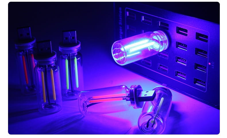 A glowing usb night light encased in a clear glass bottle with a black cap emitting vibrant purple color as an atmosphere light.