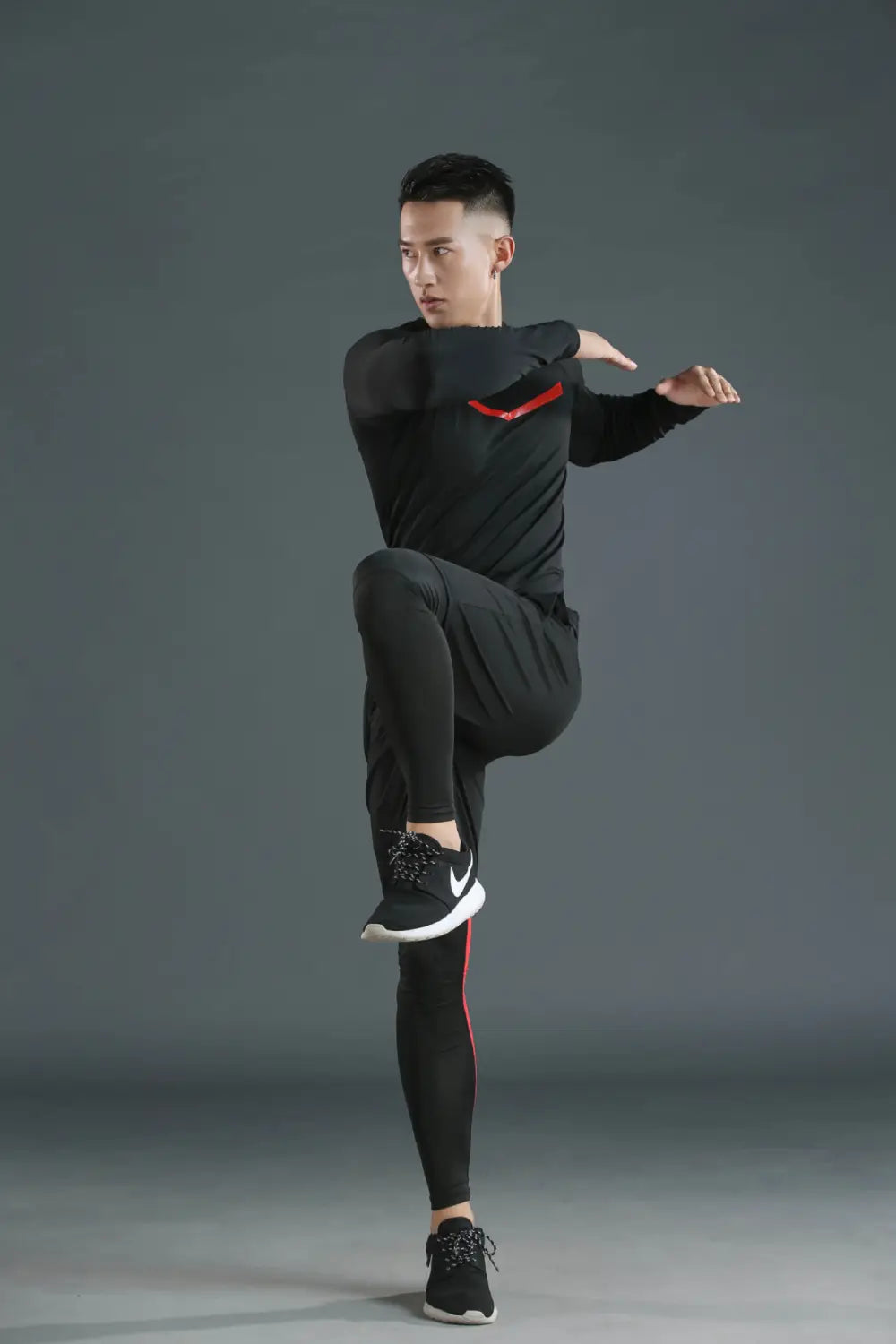 Conjunto de ropa interior térmica para hombres, con forro de lana polar y secado rápido, en color negro, con detalles de acento rojo en la manga y en el lateral de los pantalones, combinado con zapatillas negras Nike con suelas blancas.