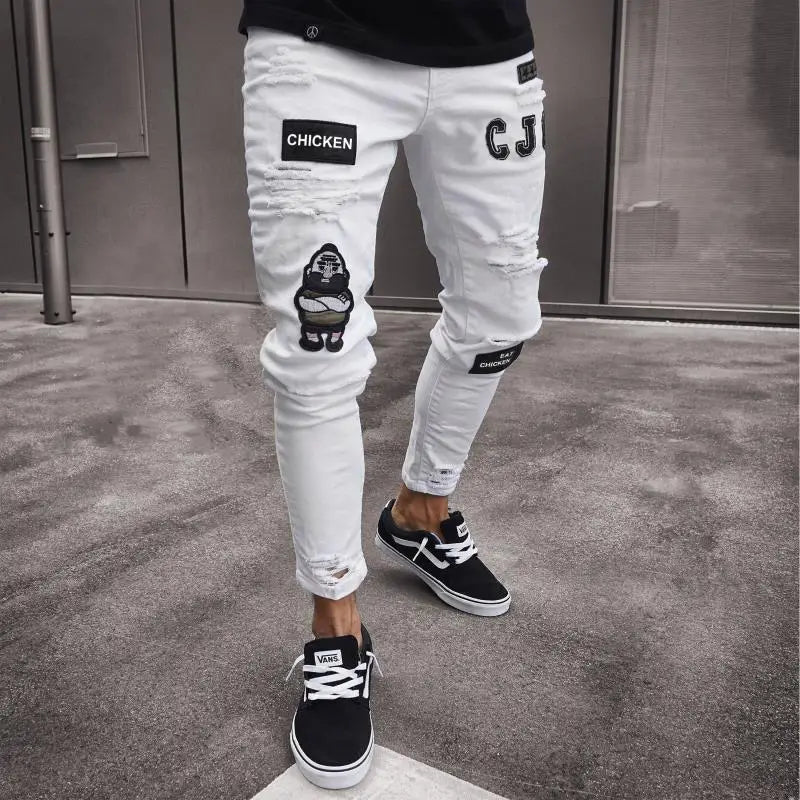 Jeans skinny déchirés slim hip-hop pour hommes, brodés, en denim blanc vieilli, avec des patchs de poulet brodés noirs et des patchs de gorille en dessin animé, associés à des baskets Vans noires.