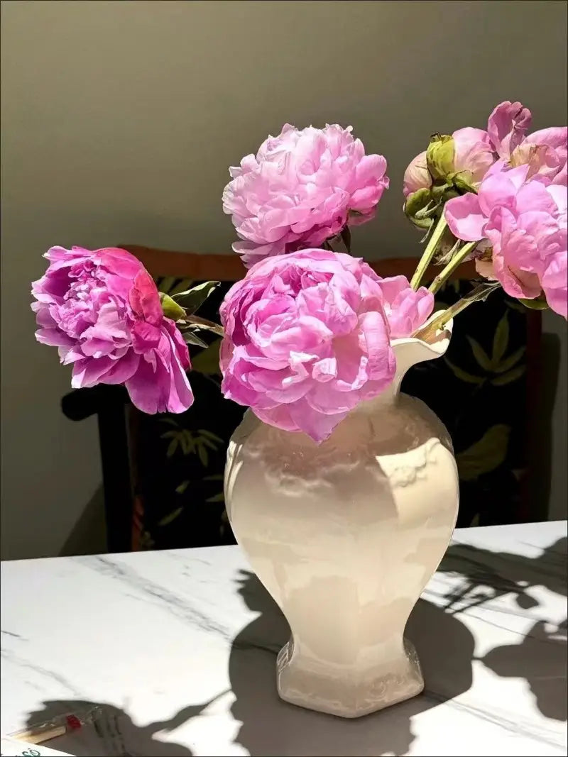 Un jarrón de cerámica moderno color crema con base acanalada y detalles discretos en relieve que sostiene vibrantes peonías rosas, ideal para la decoración del hogar con cerámica moderna francesa.