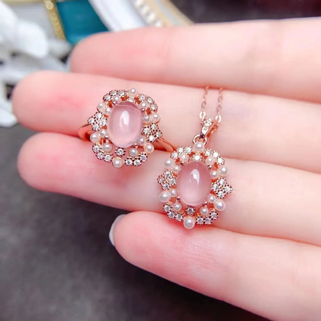 Un ensemble de bijoux en argent sterling avec quartz rose, comprenant un pendentif délicat en or rose et une bague assortie, ornés de pierres ovales en opale rose entourées de diamants étincelants et de petits perles.