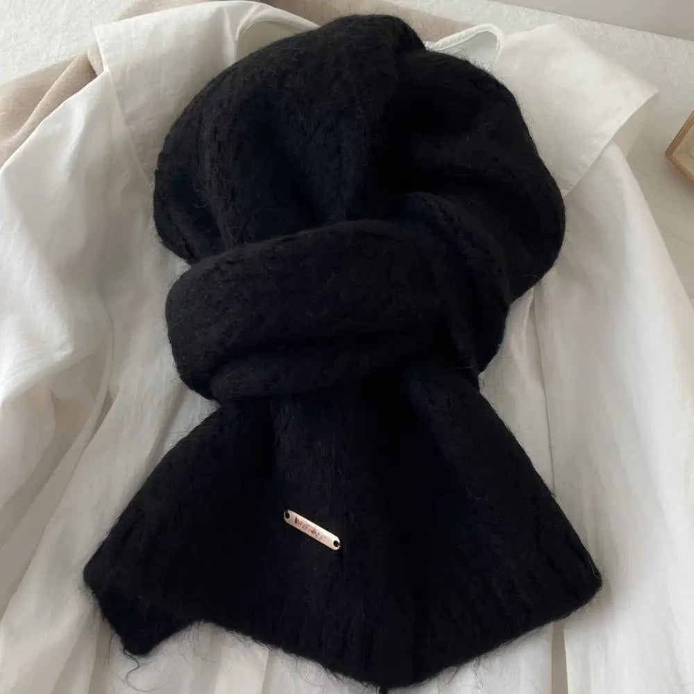 Bufanda de punto esponjosa negra con una superficie de textura suave y una pequeña etiqueta metálica, diseñada como bufanda de punto de invierno para mujer, calentador de cuello y chal.