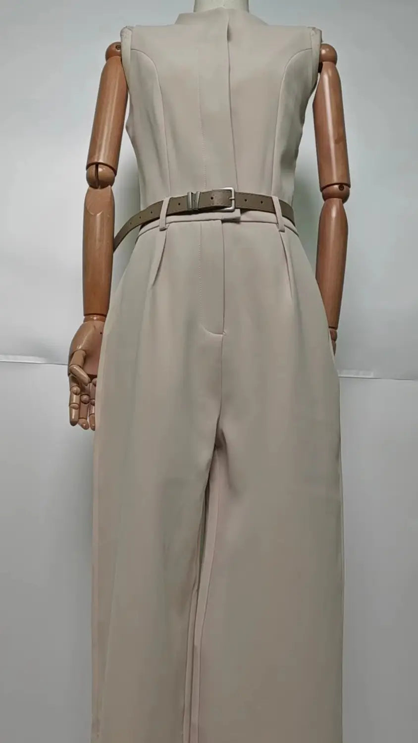 Une combinaison beige sans manches à taille cintrée et ceinture assortie, présentant un col halter et un design à jambes larges.