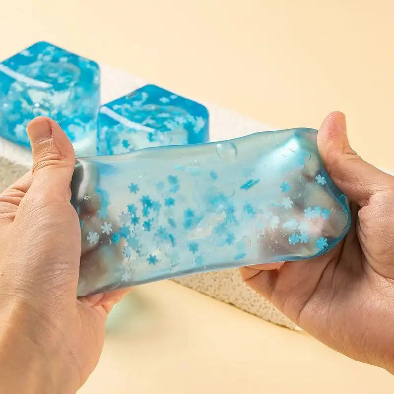 hands holding blue translucent squishy snowflake ice made of gel with embedded snowflake ice cubes glitter particles slow rising sensory fidget toy