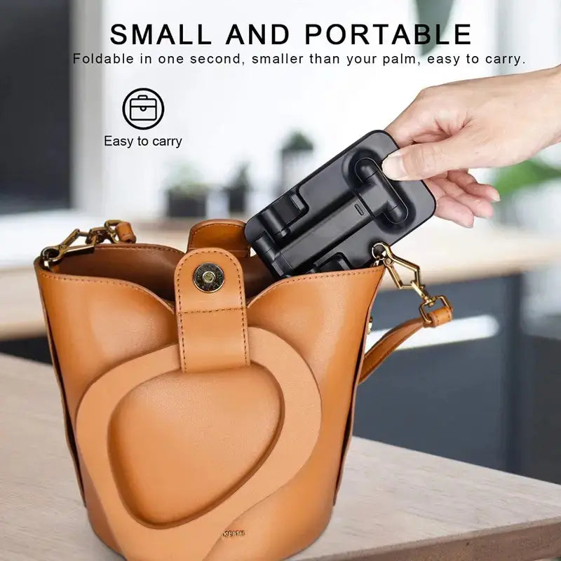 Support réglable pliable pour téléphone de bureau et tablette noir, tenu dans une main au-dessus d’un sac bac en cuir beige.