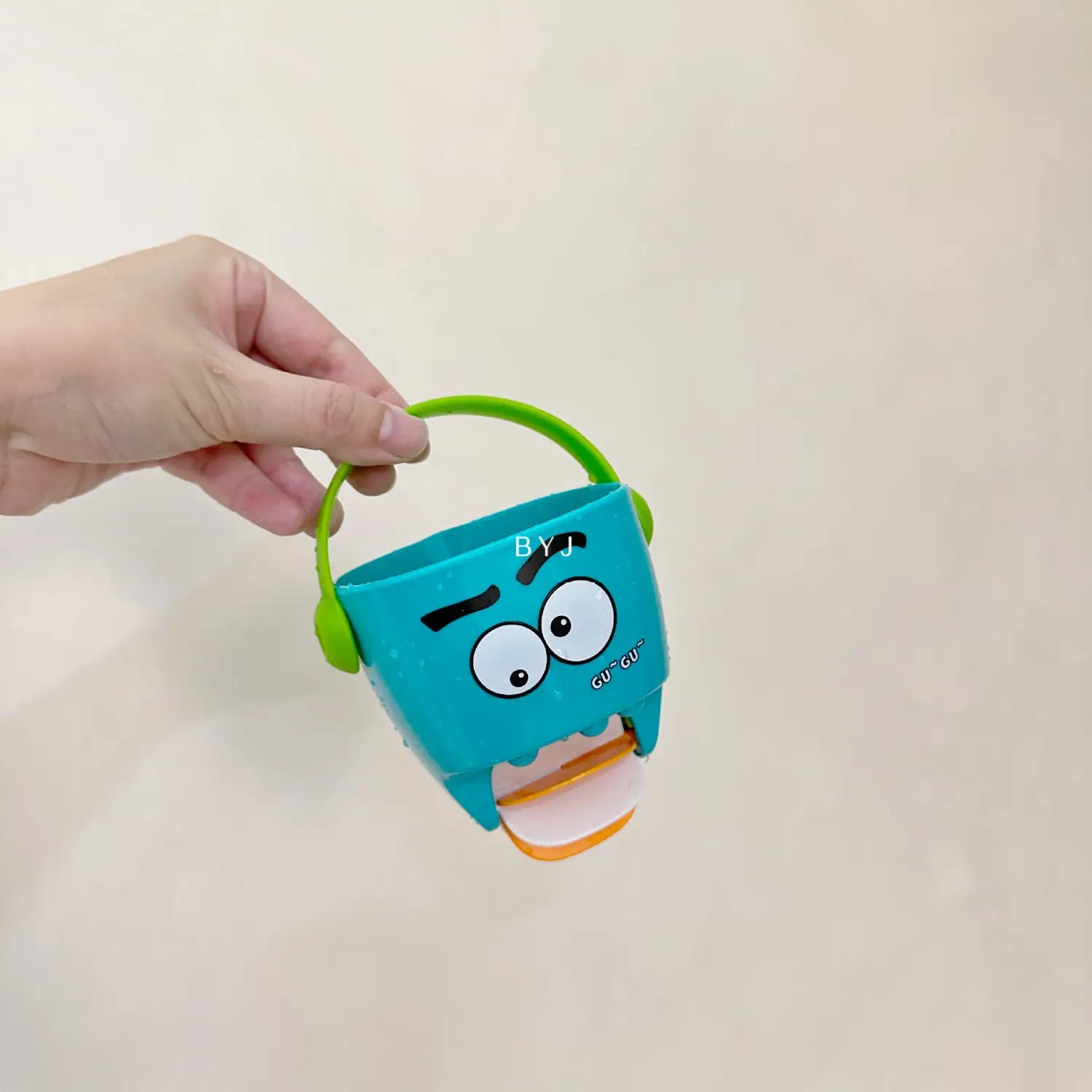 Ein türkisfarbener Kunststoff-Badewannen-Eimer für Babys mit grünem Griff und einem Cartoon-Monster-Gesicht-Design für ein Wassersprühspielset.