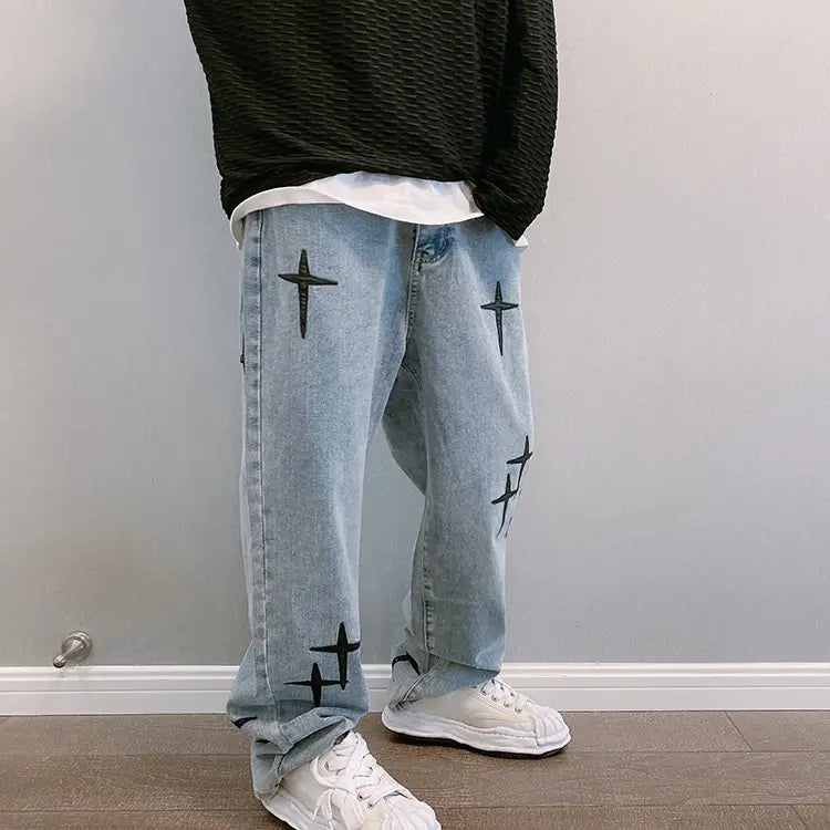 Pantalon cargo en jean à jambes larges à effet délavé clair avec broderie croisée noire sur les jambes.