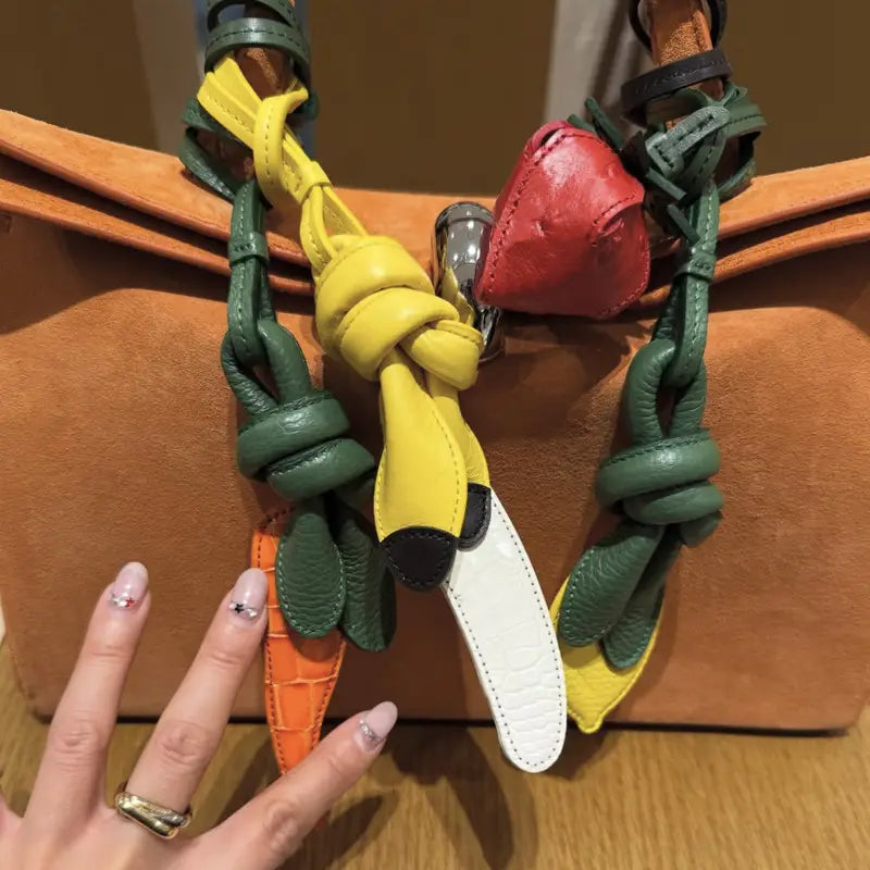 Un ensemble éclatant de charms pour sac à main en cuir végétal multicolore, présentant une banane jaune aux extrémités noires et des accents de feuilles vertes, conçu comme ornements de sac à main de créateur.