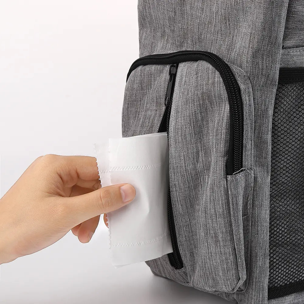 Sac de voyage pour chien en tissu gris à texture, avec fermeture éclair, comprenant une fermeture éclair noire, un panneau en mesh et une poche latérale contenant un rouleau d’essuie-tout en papier blanc.
