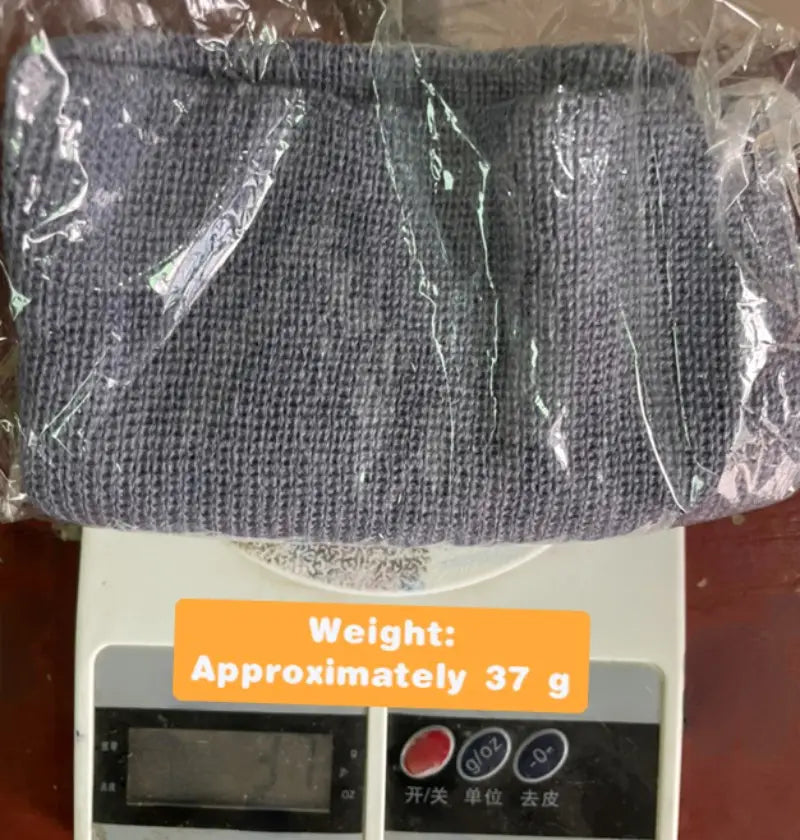 A dark gray ribbed knit winter beanie hat made of warm knitted material is wrapped in clear plastic and resting on a digital scale.
