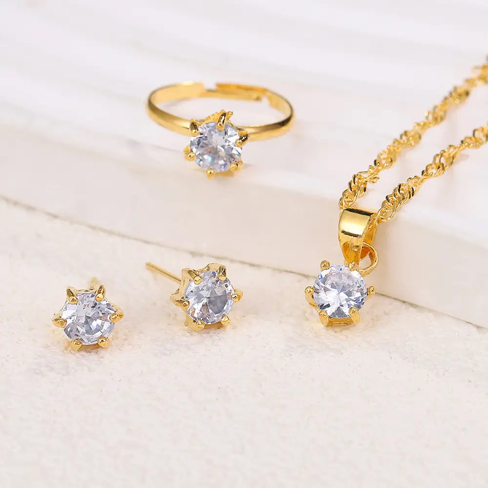 Juego de joyería de 5 piezas con circonitas cúbicas de color dorado, que presenta un collar de cadena delicado, un anillo a juego y unos aretes tipo botón, cada uno adornado con piedras facetadas transparentes.