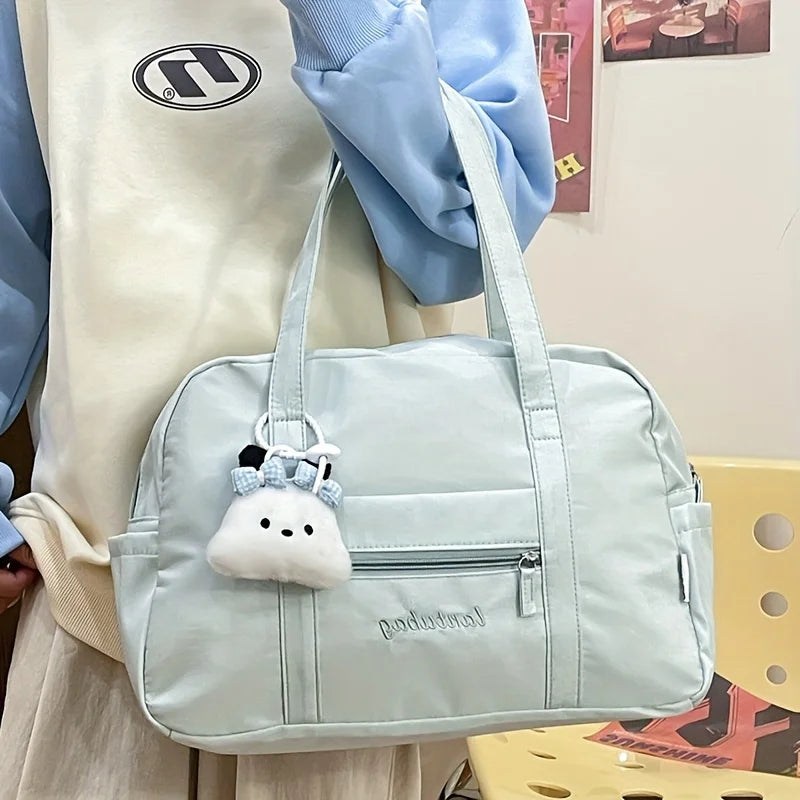 Bolsa de viaje tote de nailon acolchado color azul claro con un llavero de nube de peluche colgando de la asa.