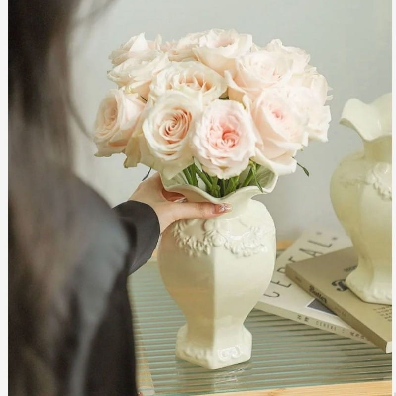 Jarrón de cerámica moderno color crema con relieve floral intrincado y un borde acanalado que sostiene un ramo de rosas suaves rosadas para una decoración elegante del hogar y un estilo de cerámica moderna francesa.