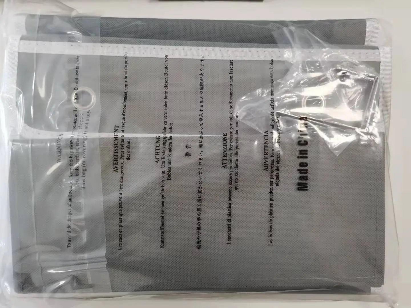 Die Rückseite der grauen Verpackung einer Gesichtsschutzmaske aus Kunststoff mit mehrsprachigen Warnhinweisen und dem Text „Made in China“ für eine Hängetasche zur Aufbewahrung mit Edelstahllaschen und aus Edelstahl.