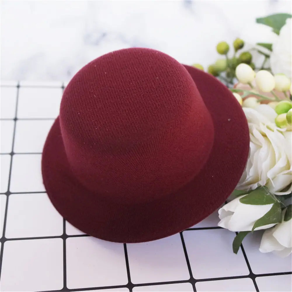 Un chapeau melon (bowler) en feutre bordeaux riche, avec une surface légèrement texturée et une calotte arrondie, conçu comme accessoire de mode pour chapeau de poupée en peluche pour des poupées de 60 cm.