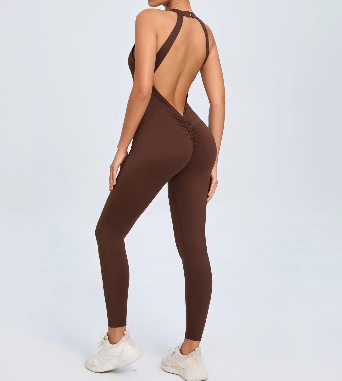 A sleek chocolate brown one-piece athletic bodysuit with a high neck open back and ruched detailing at the hips designed for workouts.