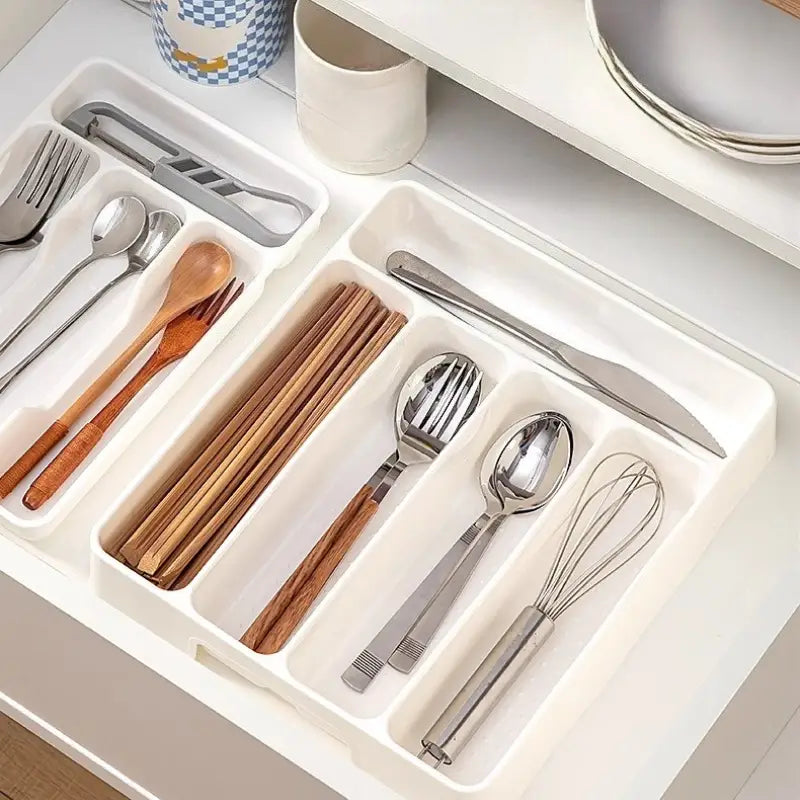Bac d’organisation réglable pour ustensiles de cuisine en plastique blanc, pour tiroir, avec compartiments segmentés accueillant des cuillères à manche en bois, des fourchettes métalliques, des couteaux, des baguettes, un fouet et d’autres ustensiles de cuisine.