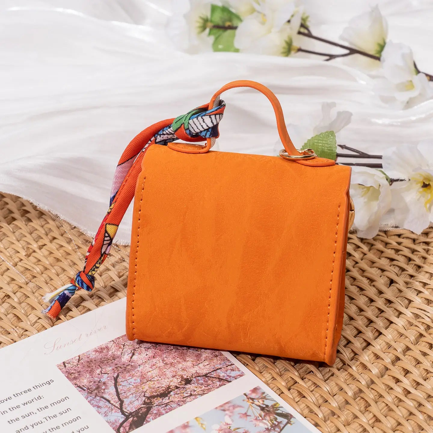 Orange miniature handbag keychain featuring a colorful patterned silk scarf tied around its handle.