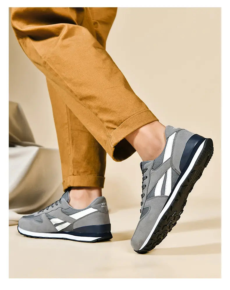 Herrenfreizeitsneaker in Grau und Weiß zum Gehen mit Wildleder-Obermaterial, schwarzer Gummisohle und markanten diagonalen Streifen.