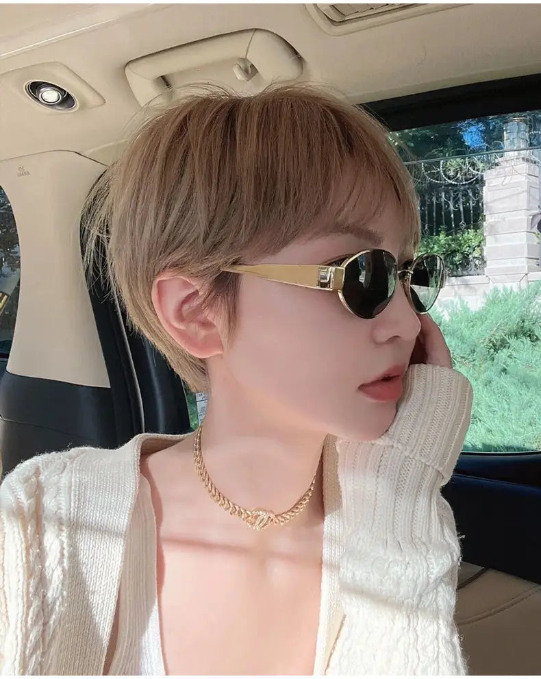 Gafas de sol ovaladas para mujer y hombre con montura dorada y lentes oscuros que presentan un diseño moderno y elegante.