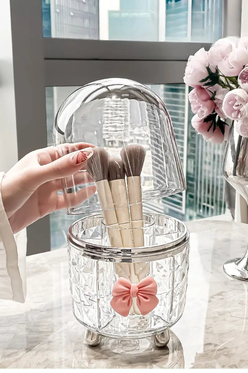 Porte-pinceaux en verre transparent avec bordure argentée métallisée et trois pieds ornés d’un nœud en satin rose, pour une boîte de rangement tournante pour maquillage et organisation des cosmétiques.