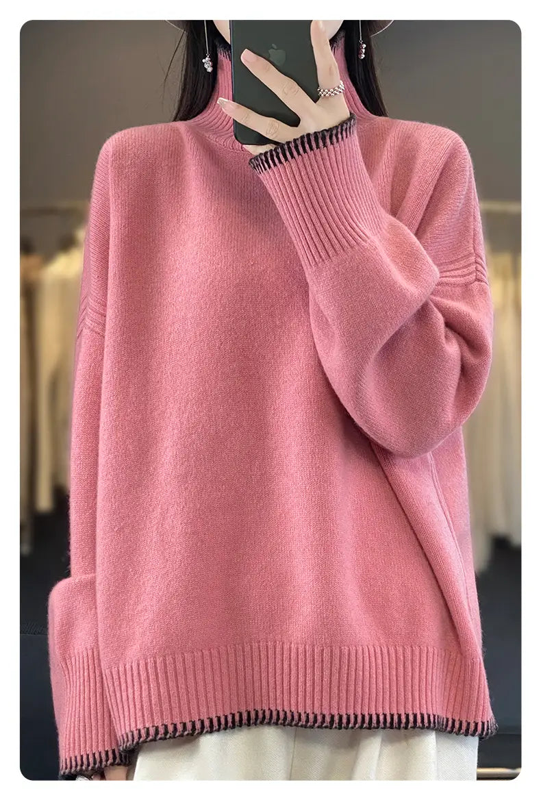 A soft pink pure wool turtleneck sweater for women featuring an oversized knit design with ribbed cuffs and hem accented by subtle black and white striped trim.