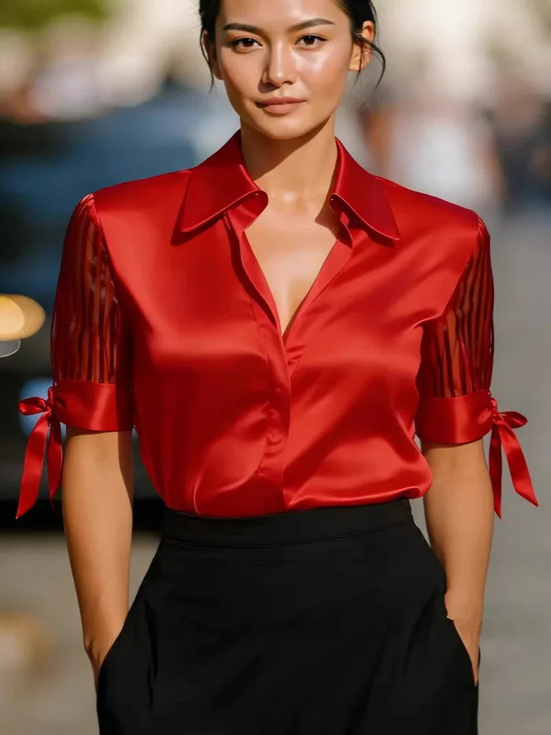 Chemisier en satin rouge vif à poignets boutonnés avec nœud, doté de manches transparentes rayées et de nœuds assortis aux poignets.
