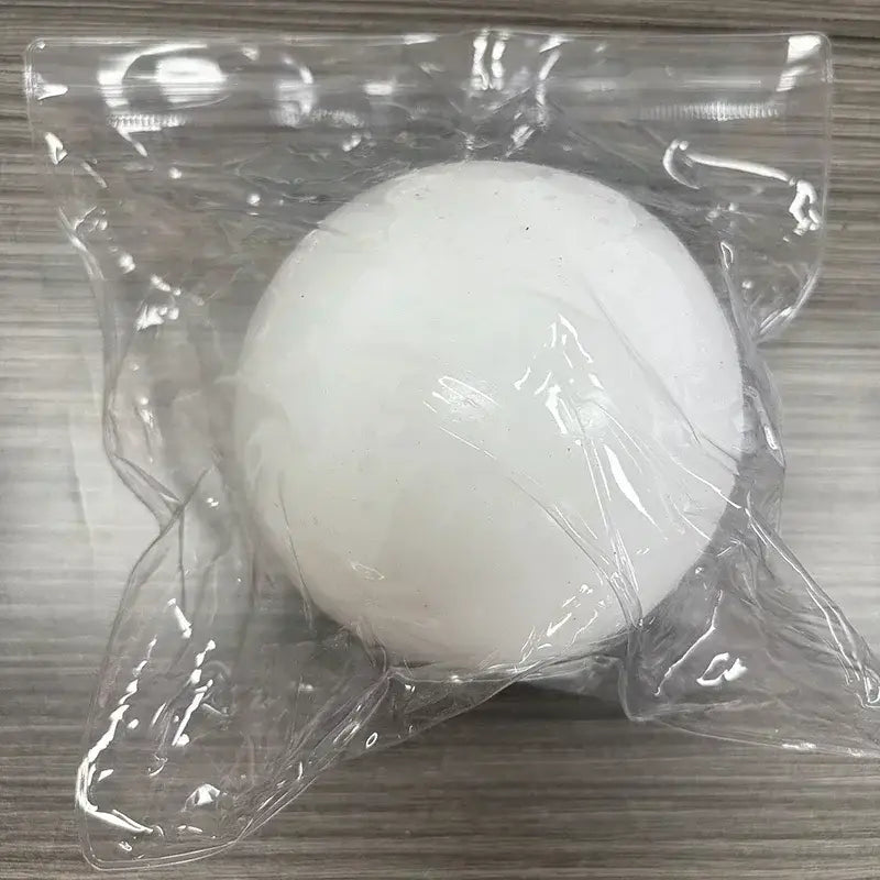 Un jouet à mâcher et à malaxer en forme de fromage sphérique blanc, solide et lisse, fabriqué dans une matière souple, enveloppé dans un emballage en plastique transparent, conçu pour soulager le stress.