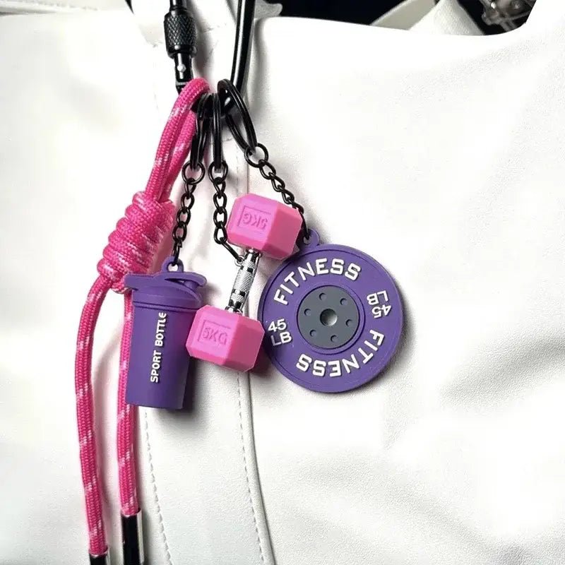 A vibrant pink and purple fitness keychain featuring miniature dumbbells, a shaker bottle charm, and a 45-pound weight plate as a colorful gym bag charm accessory.