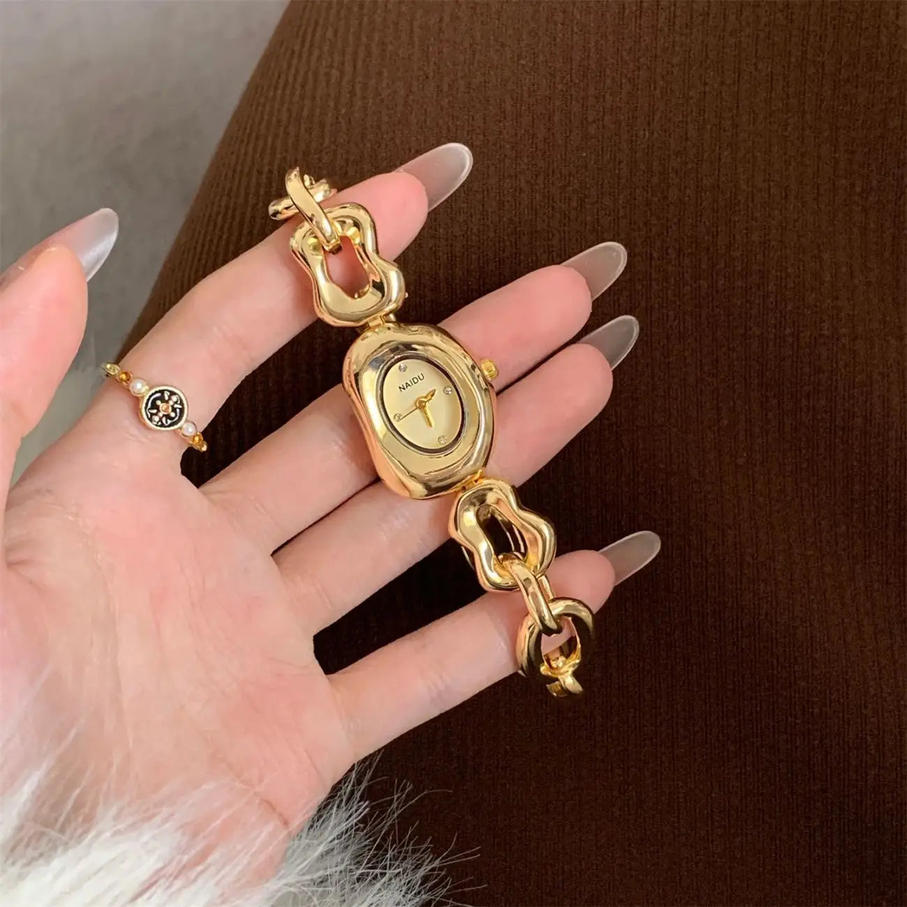 Gold-toned naiju wristwatch featuring an oval face and a chunky sculptural chain link bracelet designed as a vintage timepiece.