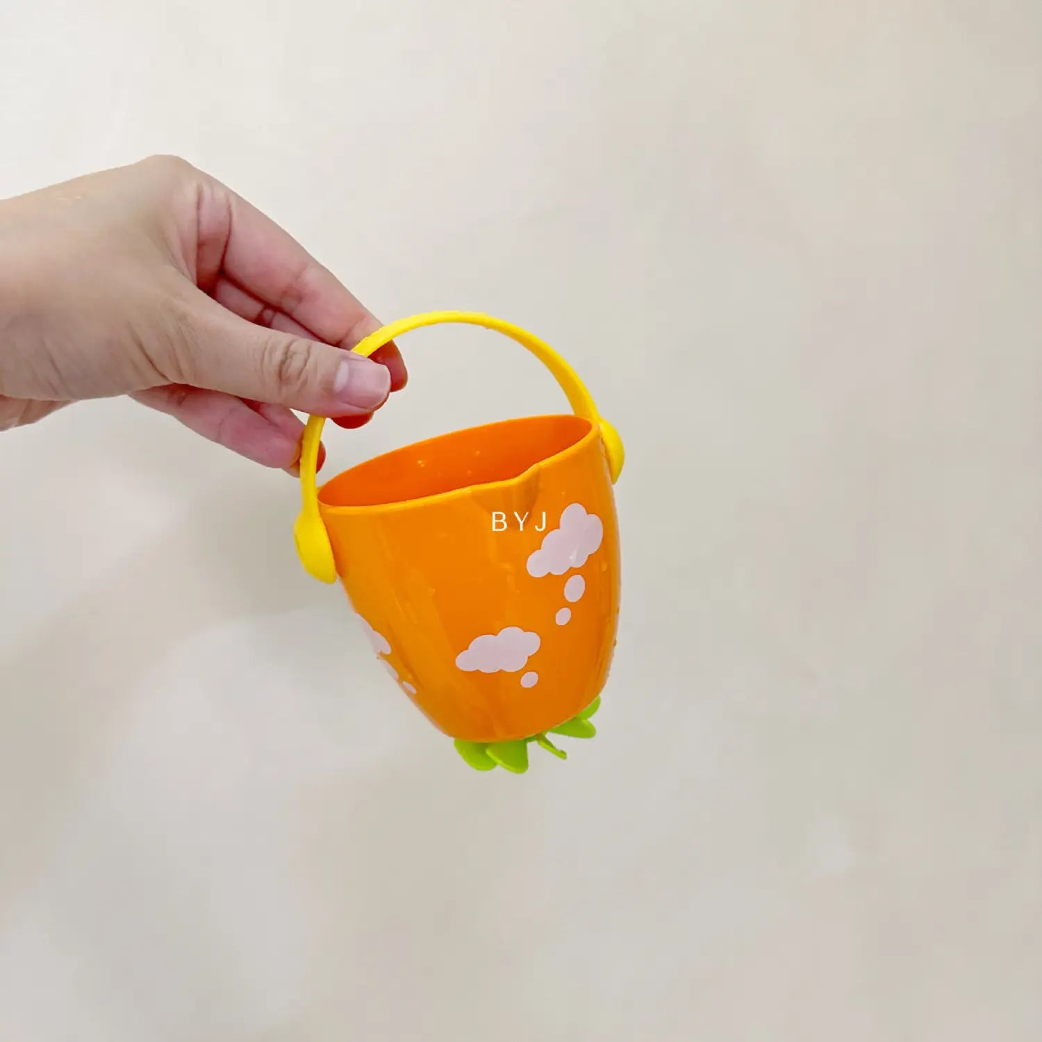 Ein orangefarbener Kunststoff-Badewannen-Eimer für Babys mit gelbem Griff und grüner, blättriger Basis, verziert mit weißen Wolkenmustern aus dem Wassersprühspielset.