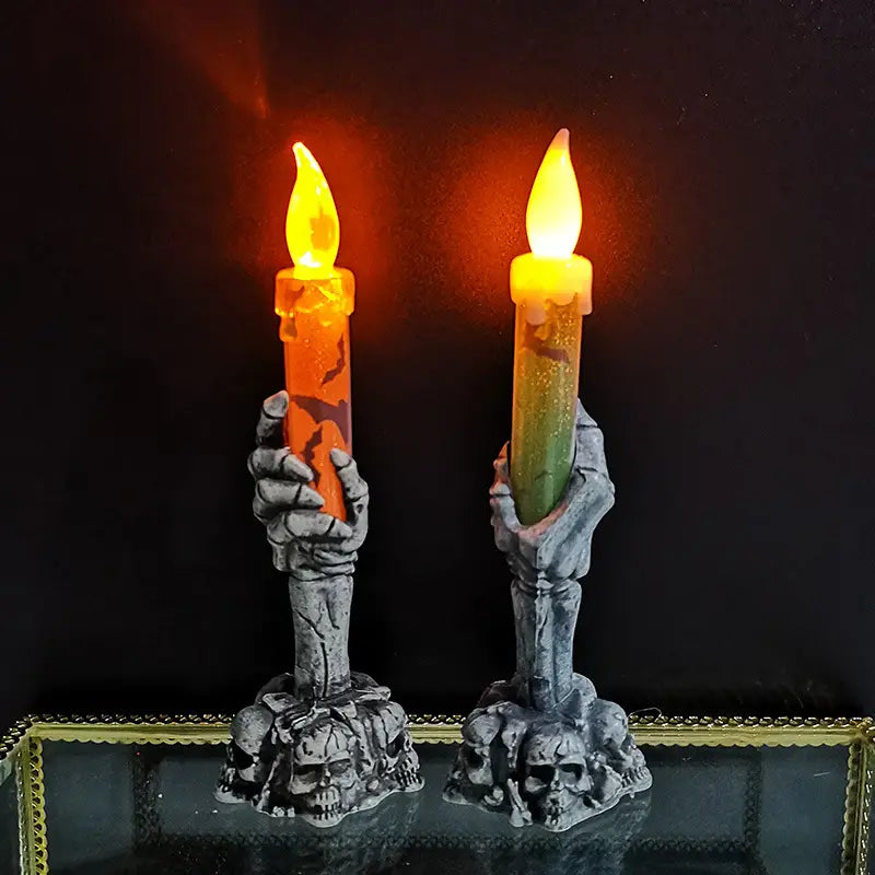 a pair of spooky skeleton hand led candle holders gripping glowing orange and green wax-like candles for a party happy halloween celebration