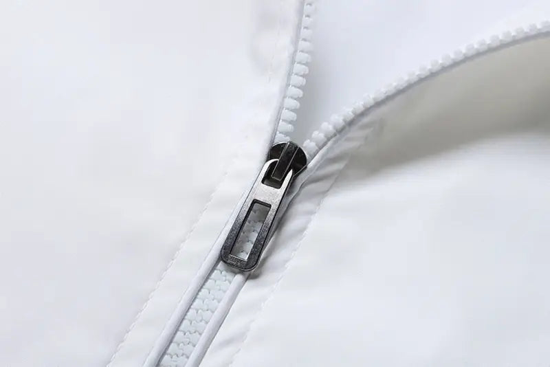 Cremallera blanca con una lengüeta metálica pulida y elegante sobre una tela blanca en la chaqueta tipo bomber USA para hombre, con gráfico de letras estilo varsity, abrigo casual