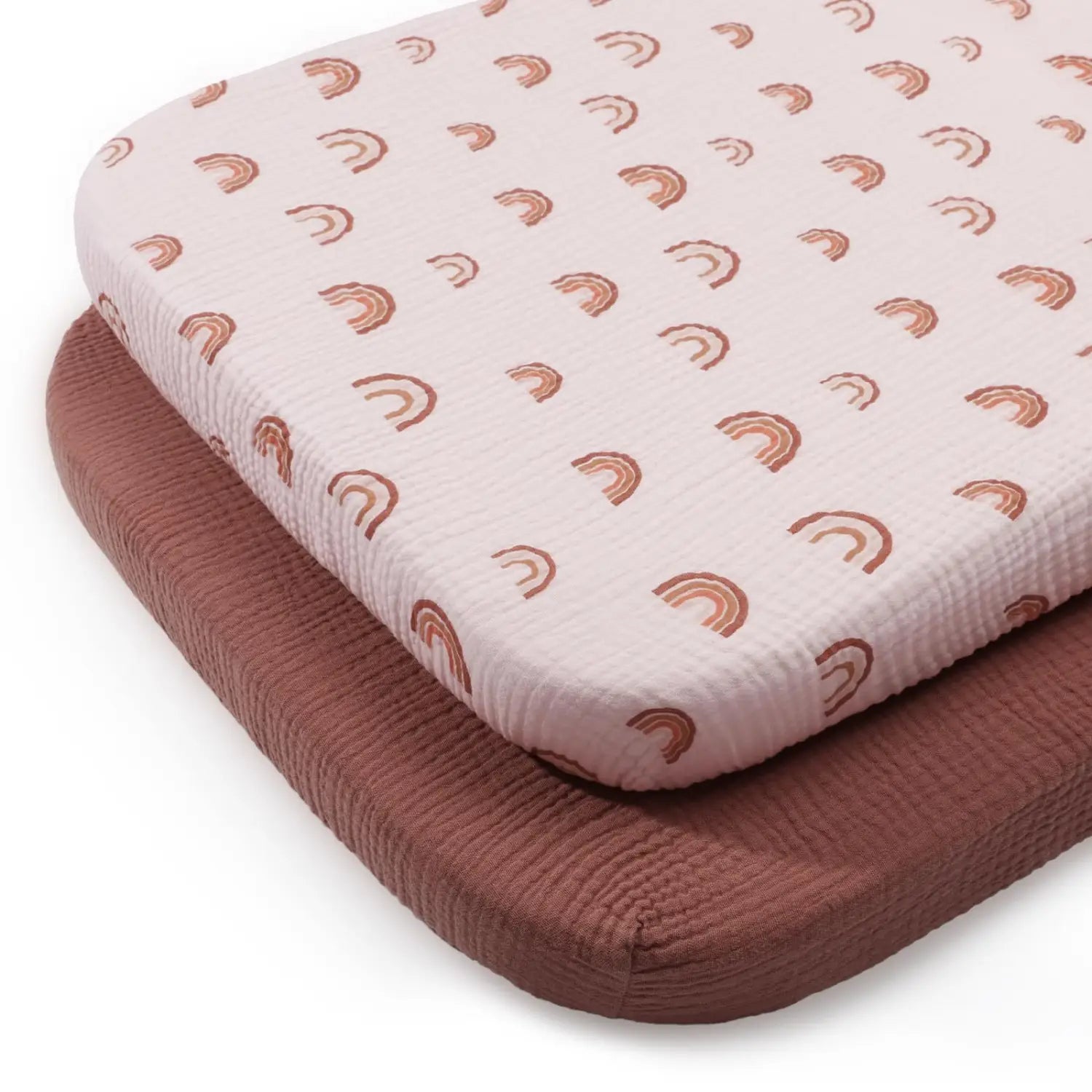 Babybettlaken-Set aus Baumwollmuslin mit einem weichen, strukturierten Stoff in hellem Rosa und einem sich wiederholenden Muster kleiner, terrakottafarbener Regenbögen.