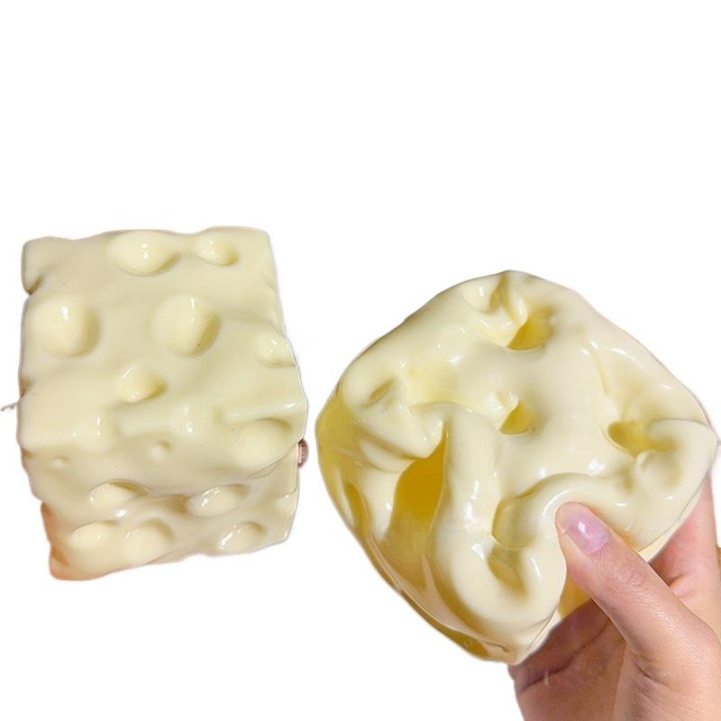 Cream-colored squishy cheese-shaped fidget toy with a glossy finish and characteristic holes for stress relief measuring 6cm by 6cm.