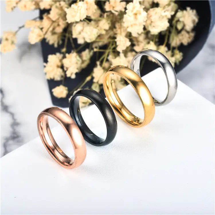 Set of four sleek polished stainless steel wedding bands in rose gold black yellow gold and silver finishes.