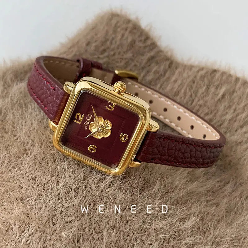 A square women quartz watch with a gold-tone case, deep burgundy floral face, and textured burgundy leather strap.