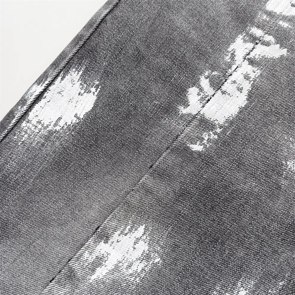 Jeans skinny déchirés pour hommes en denim gris foncé, avec un effet tie-dye déchiré, présentant des taches blanches et gris plus clair.