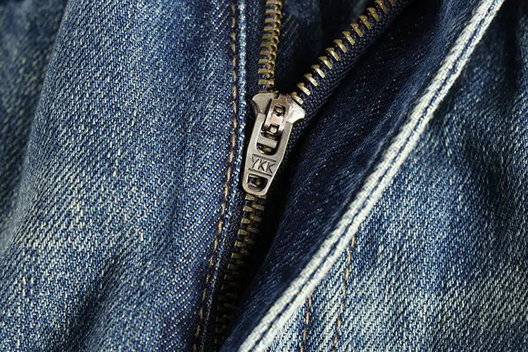 Une fermeture éclair argentée YKK avec une languette métallique sur un tissu en denim bleu foncé de jeans en denim ample à broder pour hommes.