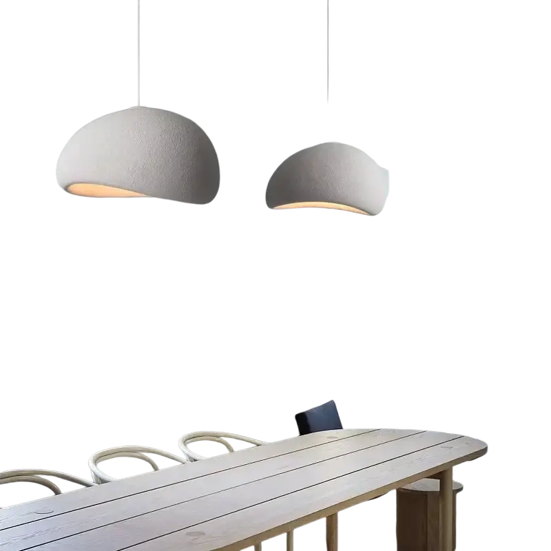 Dos luminarias colgantes blancas minimalistas con pantallas de forma de cúpula cuelgan sobre una mesa de comedor de madera en un entorno de sala y comedor.