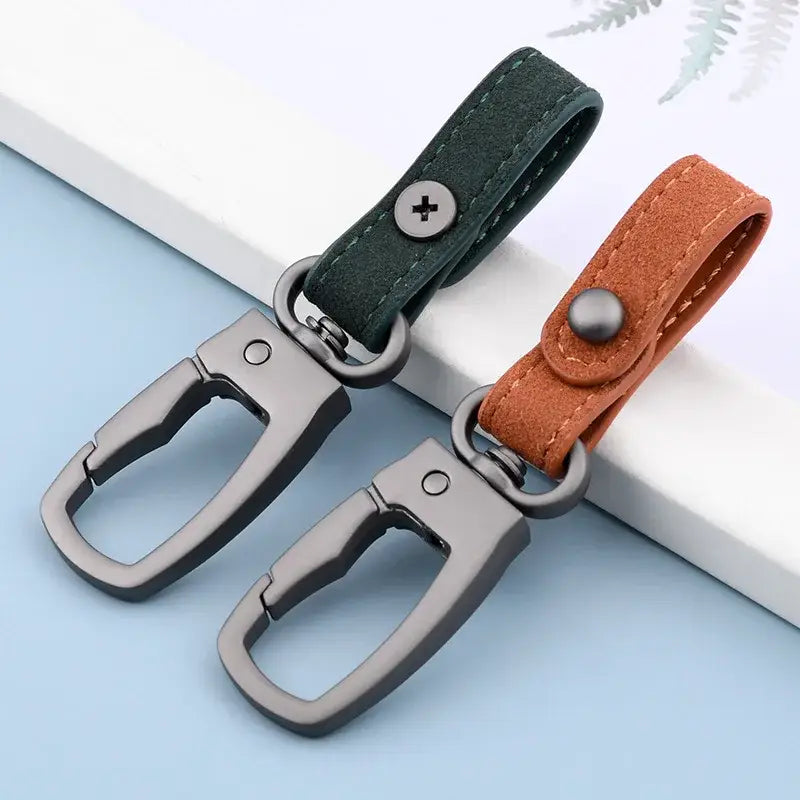 Zwei Leder-Schlüsselanhänger-Organizer für Autotasten in Dunkelgrün und Tan-Suede mit mattschwarzen Metall-Karabinerhaken und Druckknopf-Verschlüssen.
