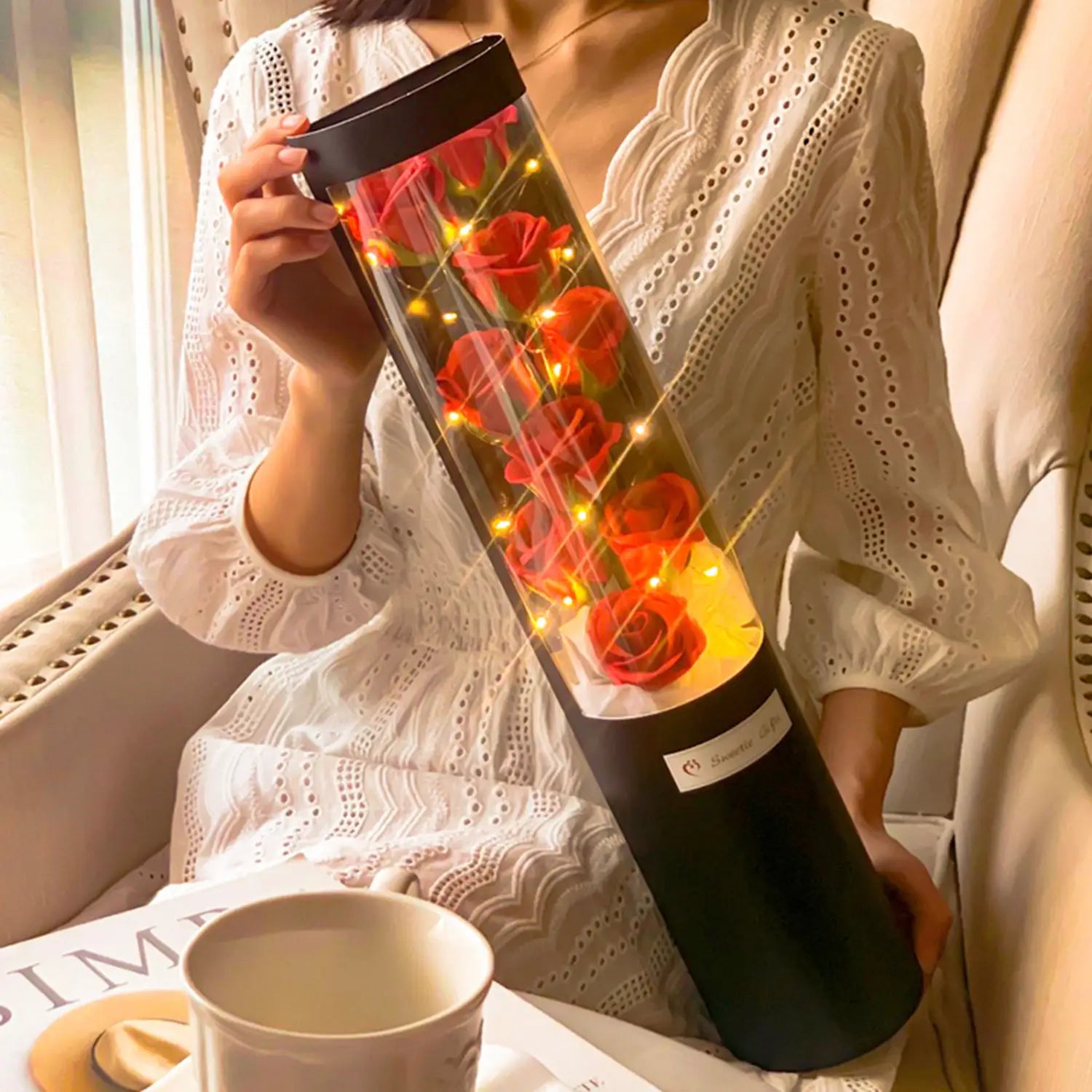 Eine zylindrische schwarze LED-Rosen-Seifenblumen-Geschenkschachtel mit leuchtenden roten Rosen, die von warmen Feenlichtern für den Valentinstag beleuchtet werden