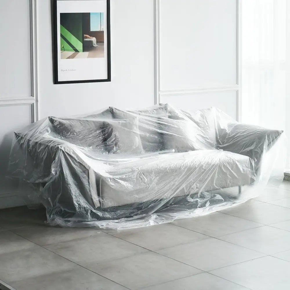 Graues gepolstertes Sofa, mit einer transparenten Kunststoff-Möbel-Staubabdeckung als Schutzhülle abgedeckt, zum Schutz vor Schmutz und Beschädigungen.