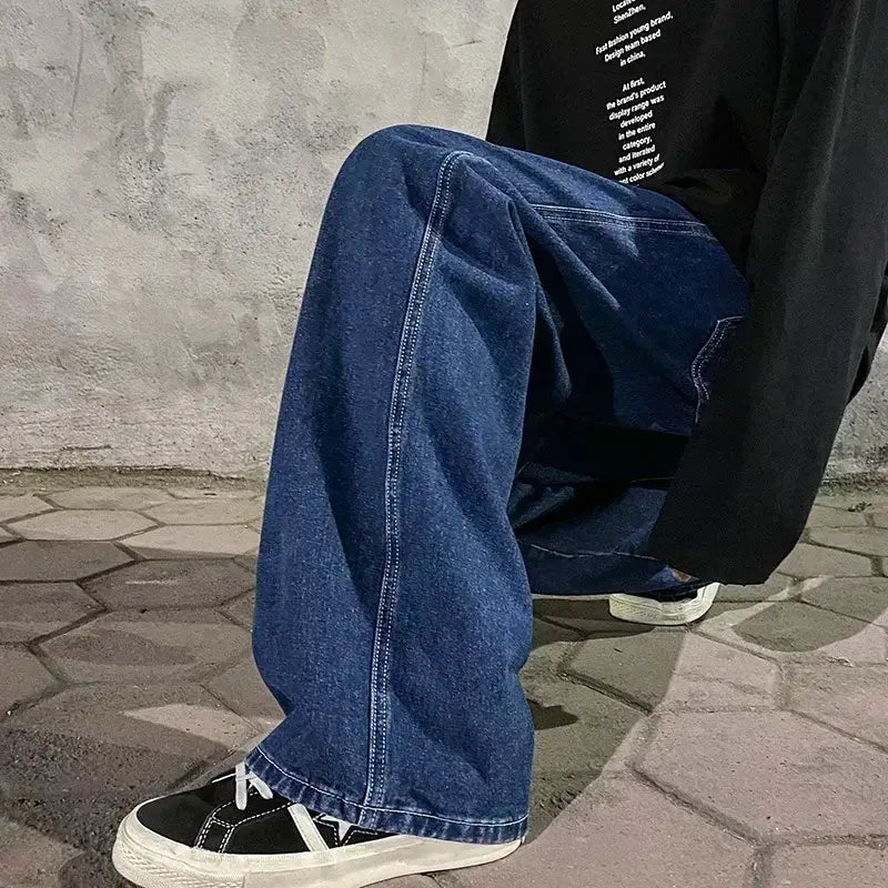 Jeans en denim bleu foncé à jambes larges pour hommes, avec une coupe ample et décontractée, des surpiqûres visibles le long des coutures, conçues dans un style streetwear coréen.