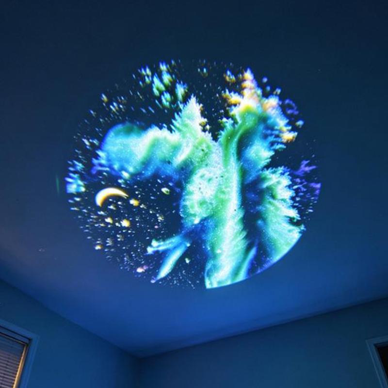 a usb galaxy projector displaying a vibrant cosmic projection with swirling blue and green nebulae accented by golden stars and a crescent moon using replaceable projection discs
