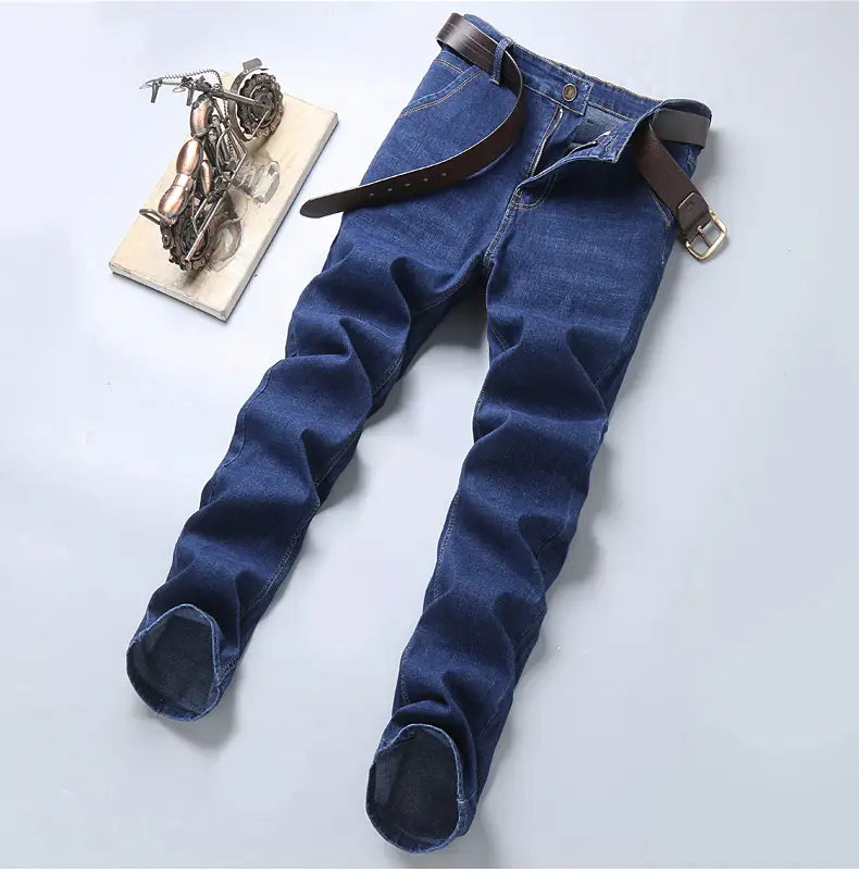 Jeans en denim extensible à coupe slim pour hommes en bleu foncé, avec une ceinture en cuir marron passée dans la taille.