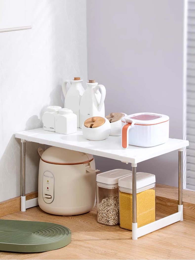 Étagère de séparation à couches en plastique blanc avec des pieds métalliques supportant la vaisselle et des contenants de rangement, conçue comme une étagère de séparation à couches réglable et un support télescopique pour évier