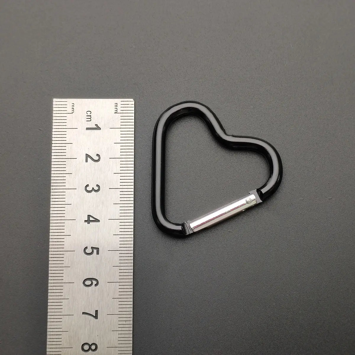 Schwarzer herzförmiger Karabinerhaken-Schlüsselanhänger mit einem silberfarbenen Verriegelungsmechanismus für eine sichere Befestigung.