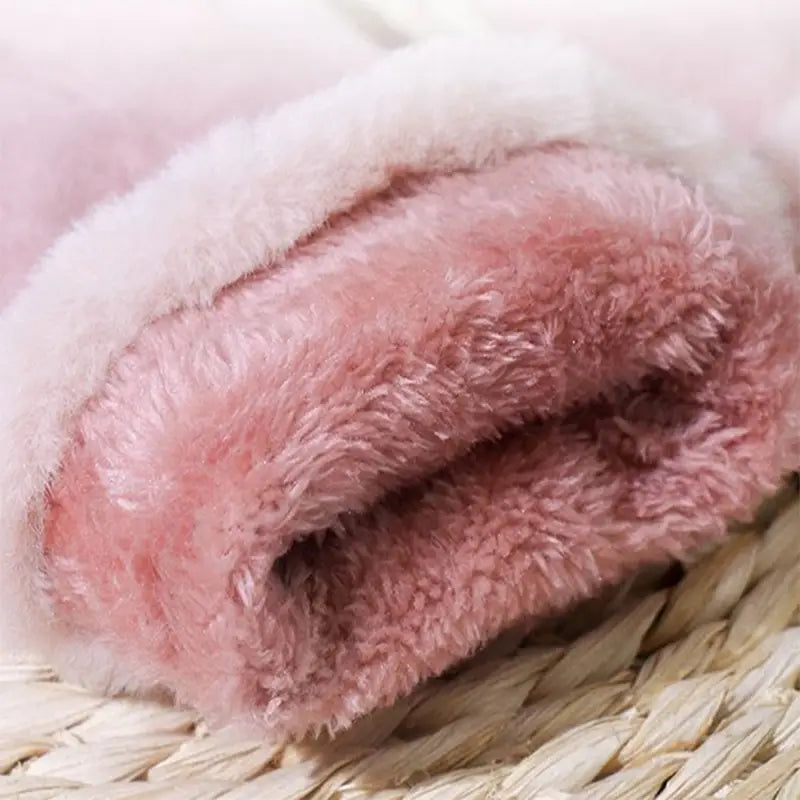 Une couverture en tissu polaire duveteux rose tendre, avec une doublure intérieure blanche contrastante, présentée aux côtés de gants chauds pour écran tactile d’hiver pour femmes